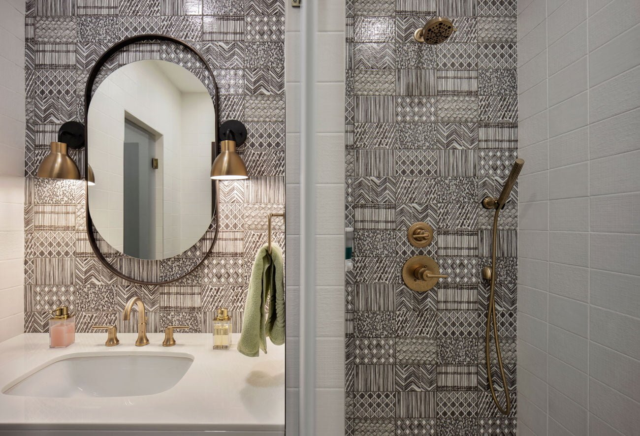 фото туалетной комнаты с плиткой с абстрактным рисунком за зеркалом и в душевой
